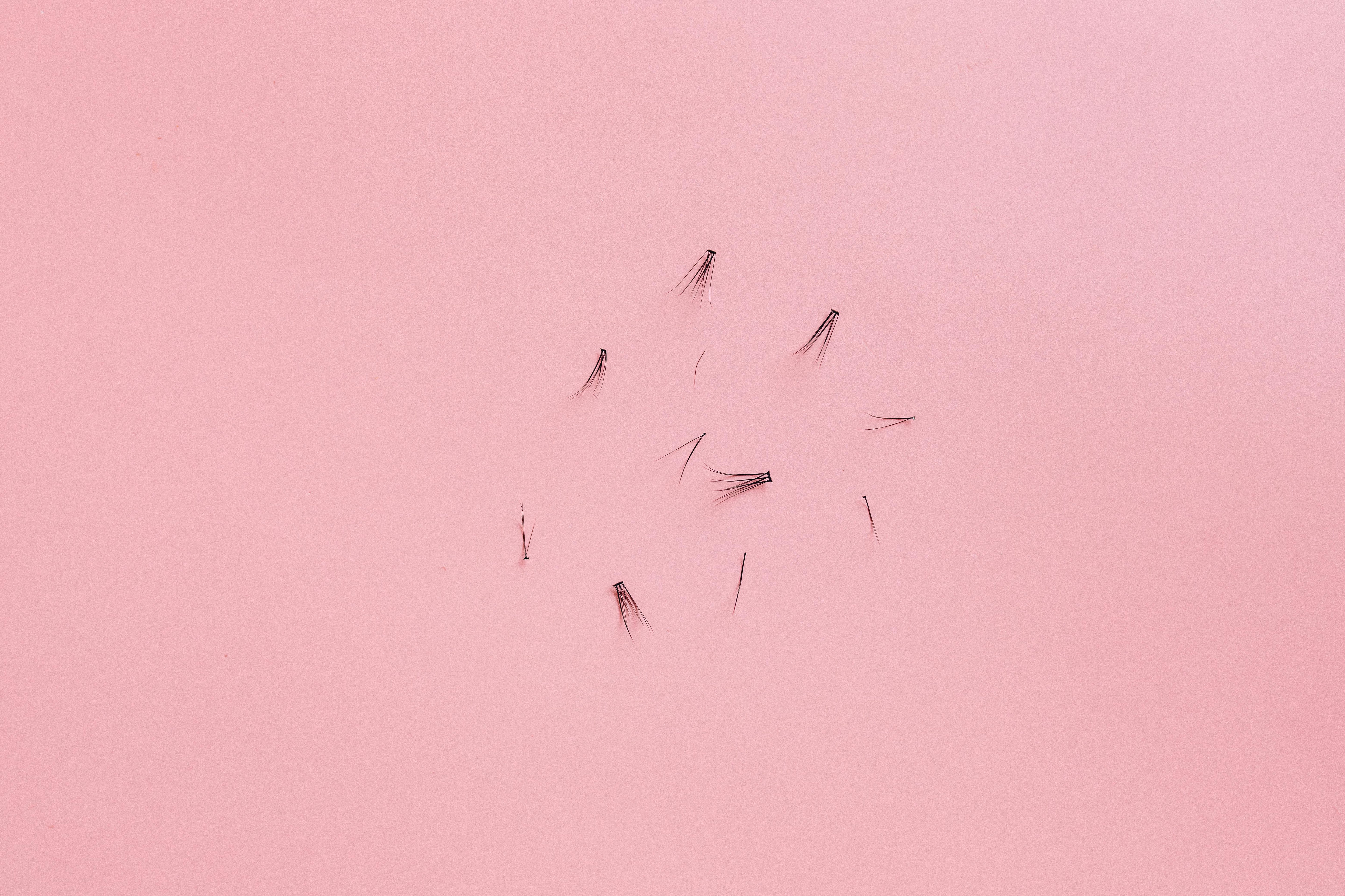 Close-up of individual eyelash extensions on a pink background, perfect for DIY lash application at home.