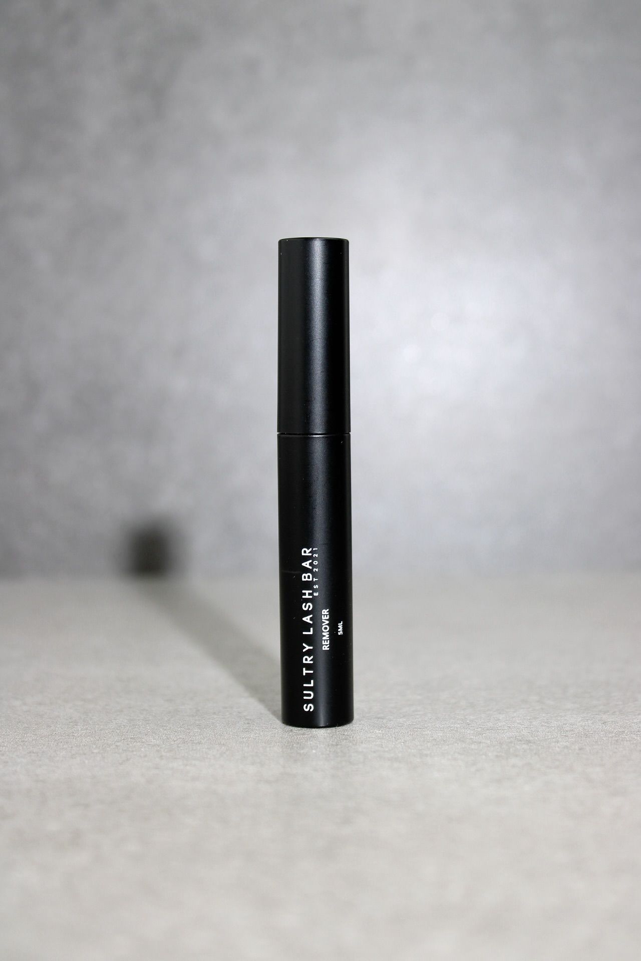 Black mascara tube on a textured surface with a gray background