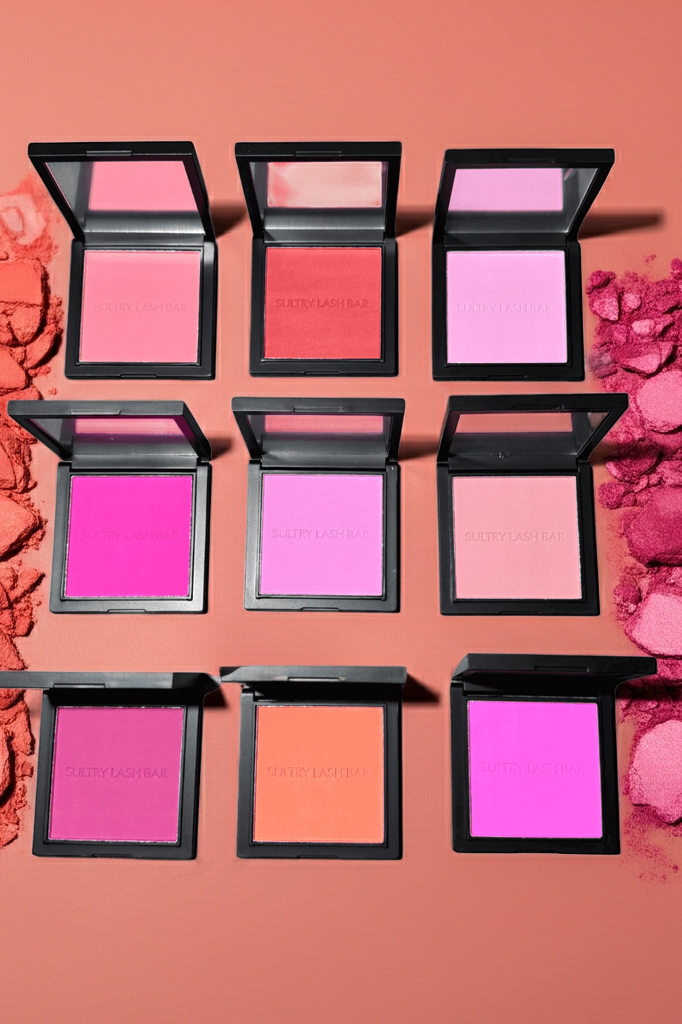 Various pink blushes in open cases with scattered blush on a pink background