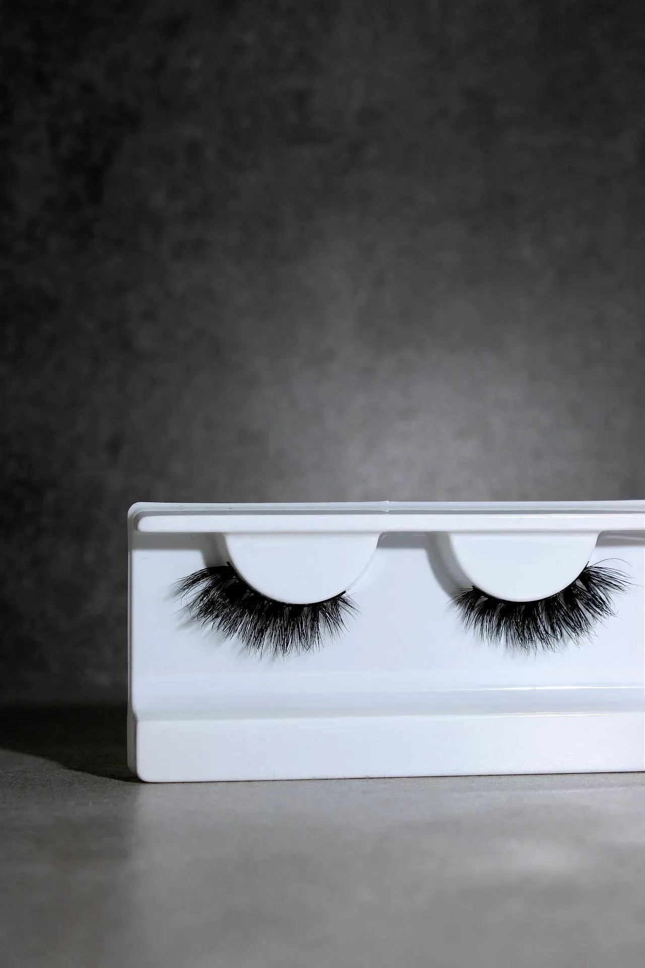 Pair of false eyelashes on a white tray against a dark background