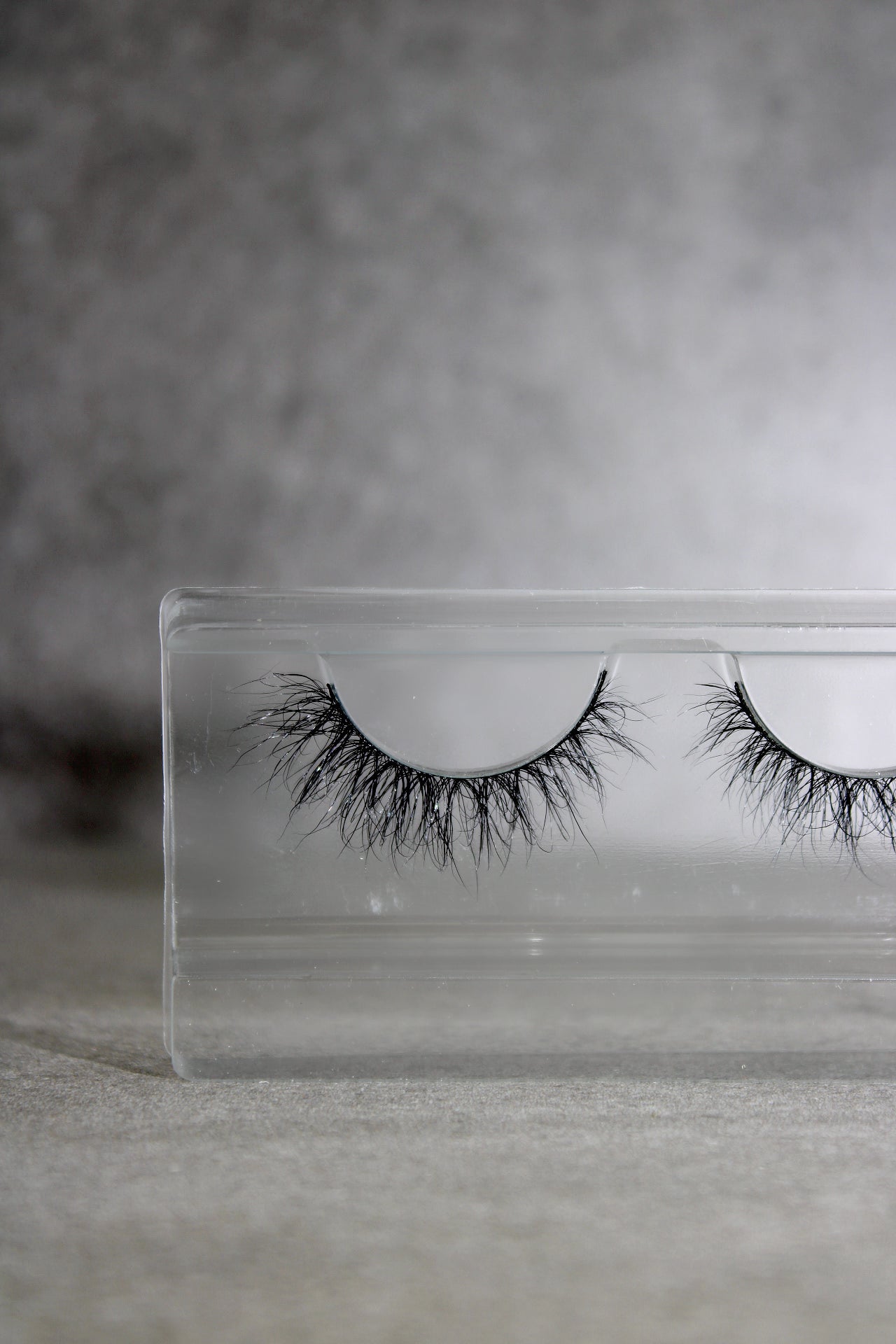 Pair of false eyelashes in a clear packaging case on a gray background