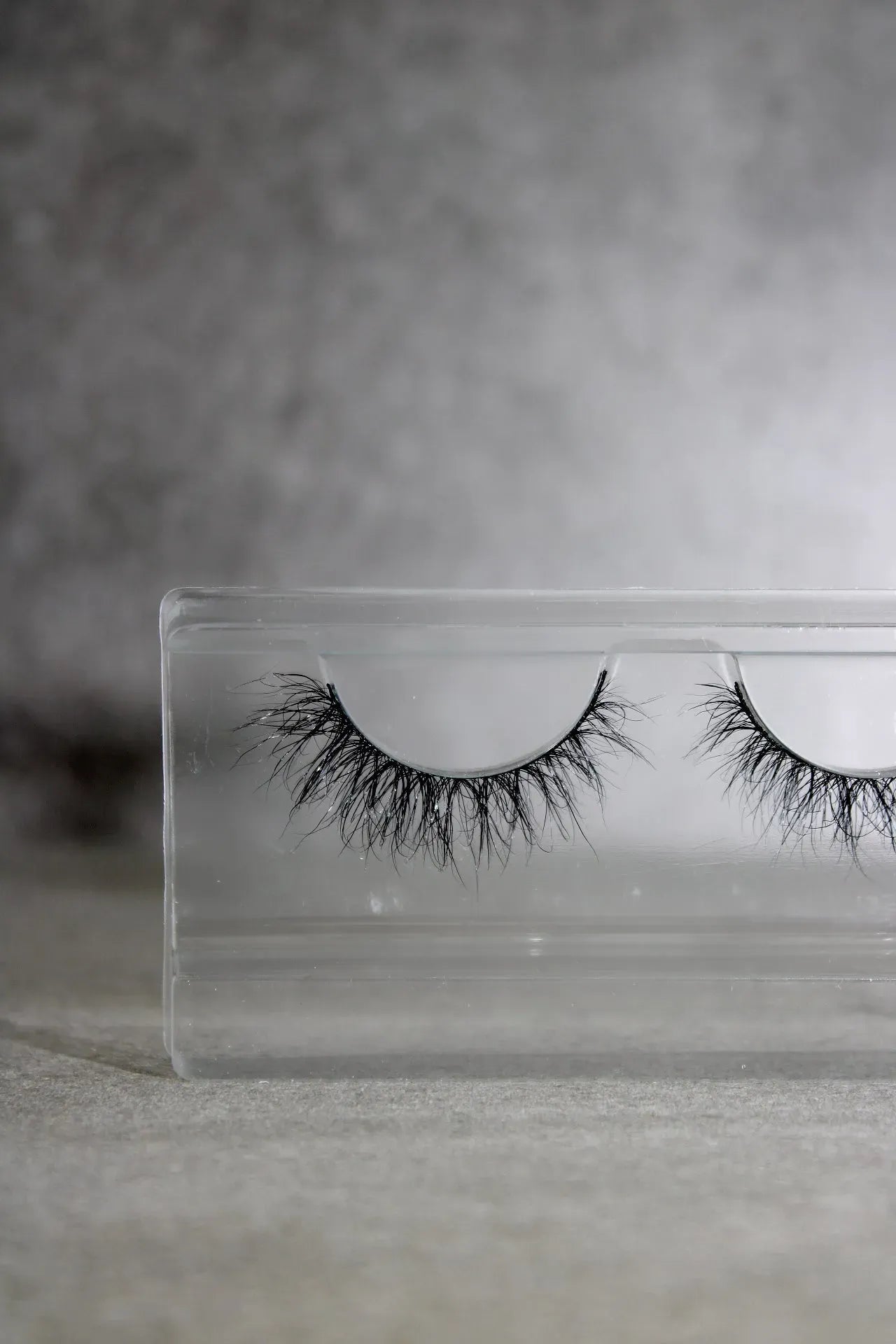 Pair of false eyelashes in a clear packaging case on a gray background