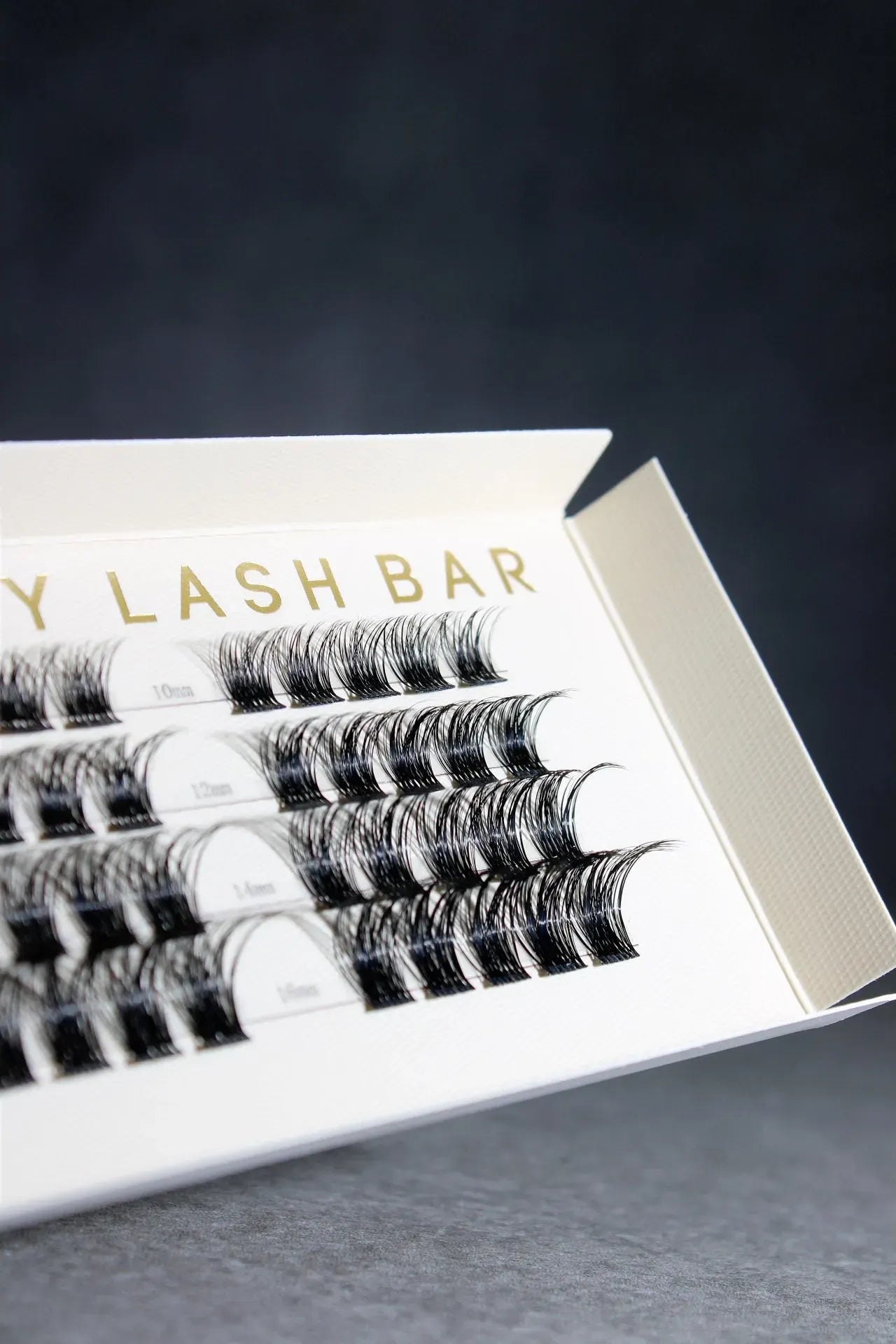 Eyelash extensions in a box labeled 'Y LASH BAR' on a dark background