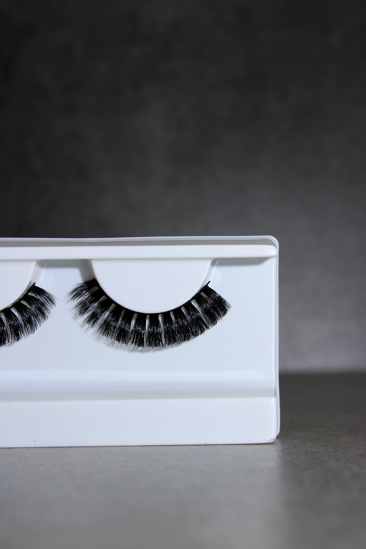 Pair of false eyelashes on a white tray against a dark background