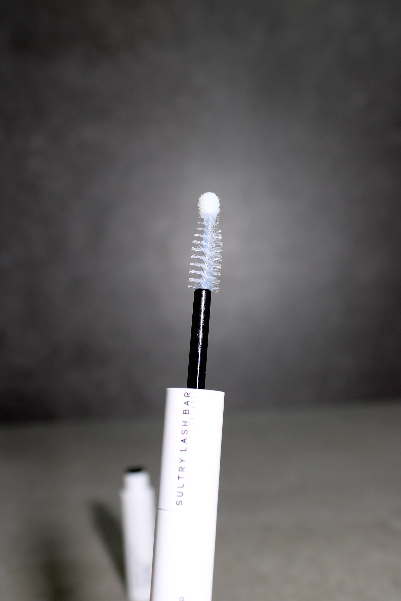 Eyelash sealer with brush applicator on a dark background