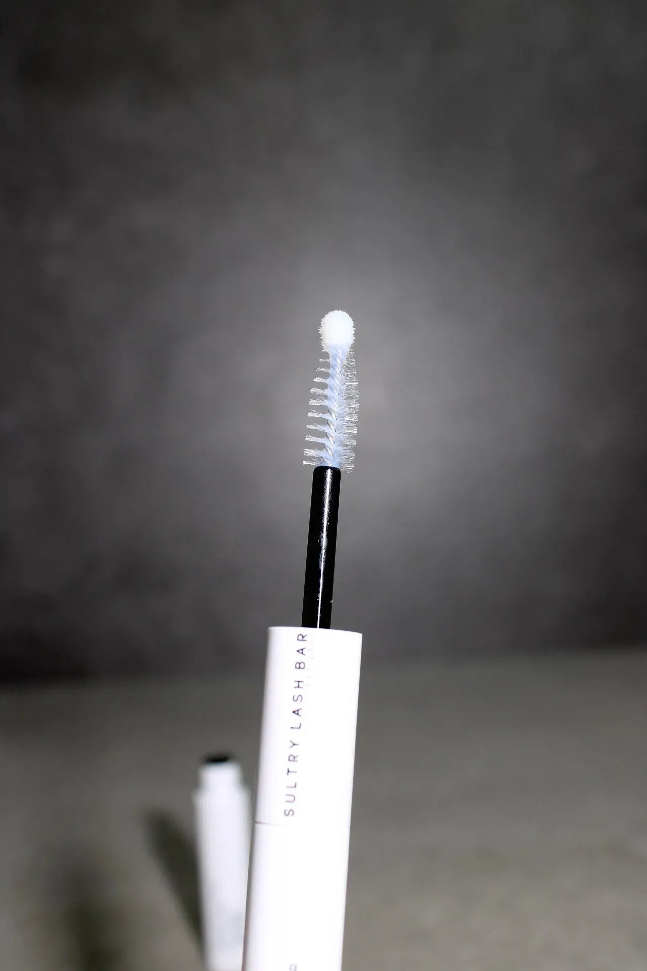 Eyelash sealer with brush applicator on a dark background