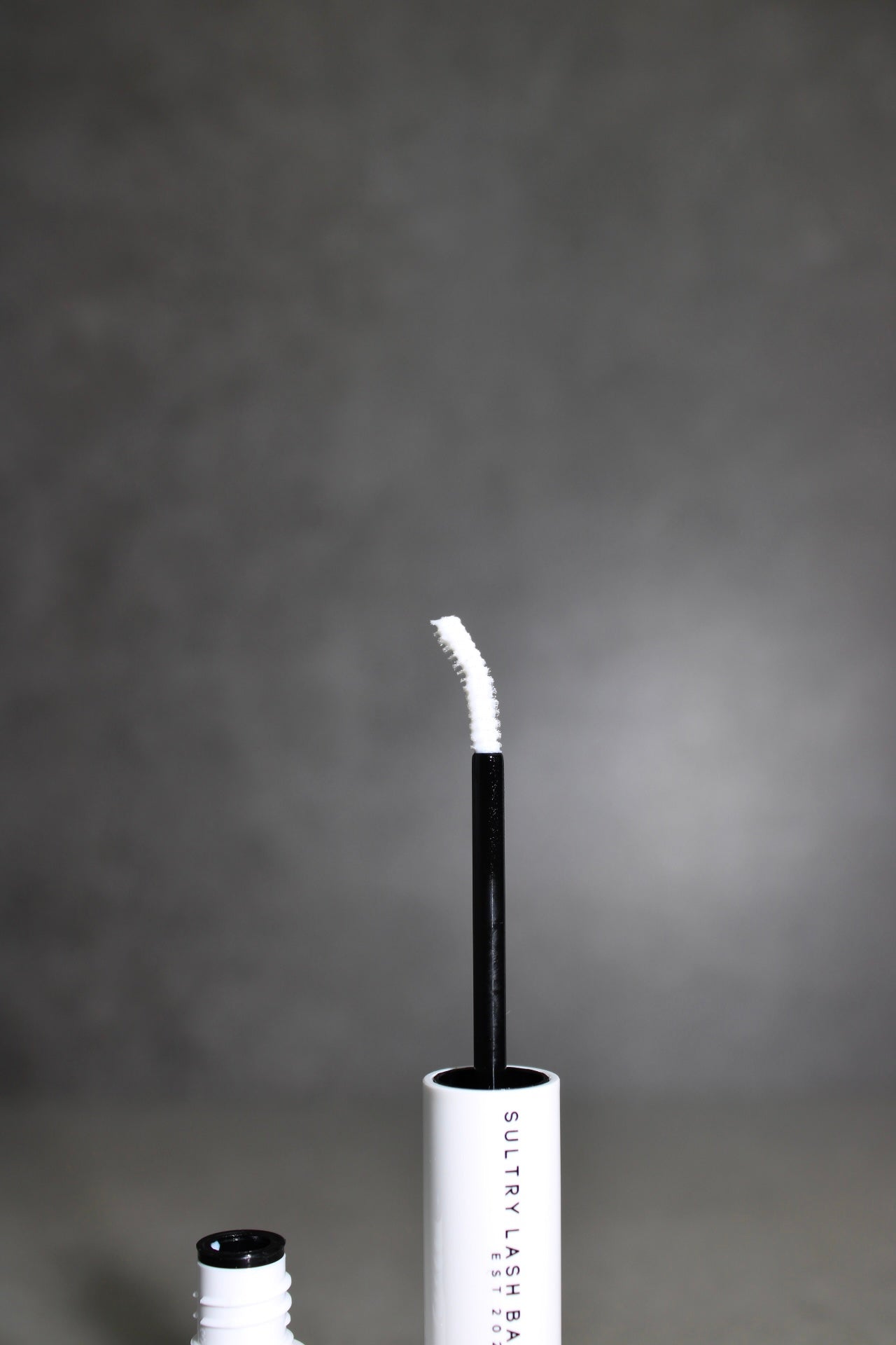 Lash extension with applicator and container on a gray background