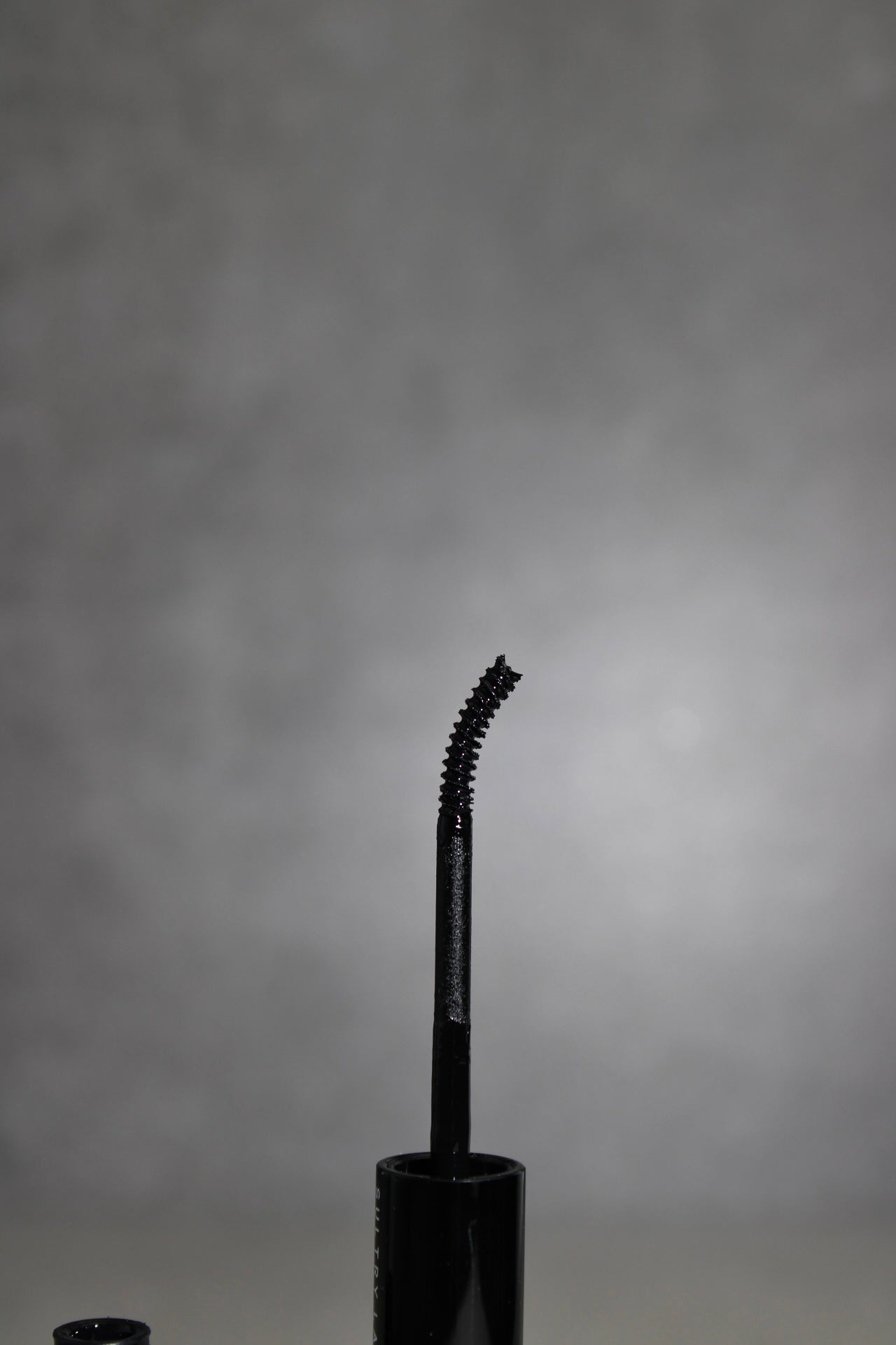 Black BOND mascara wand on a gray background