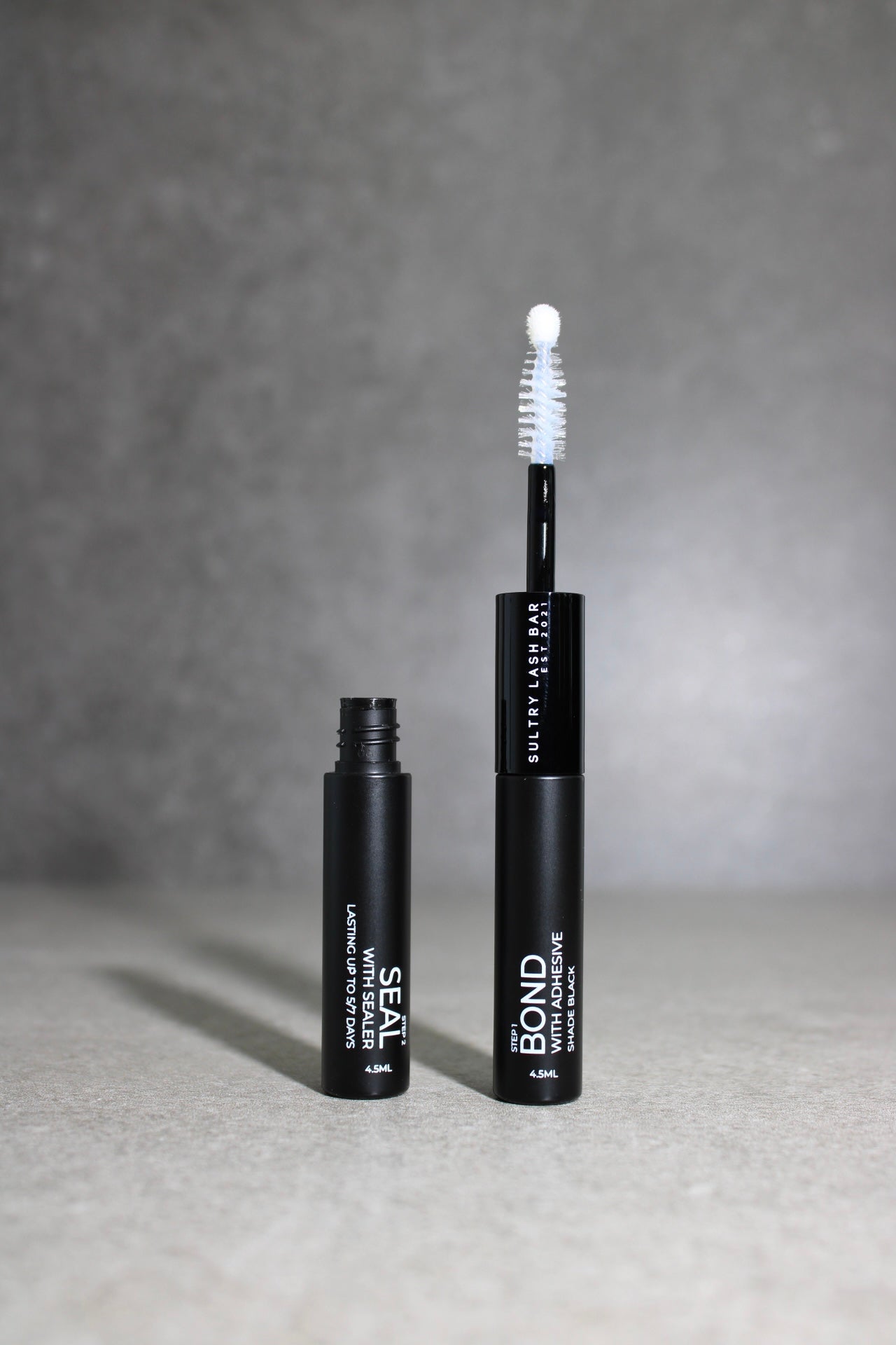 Black eyelash product with applicator on a gray background