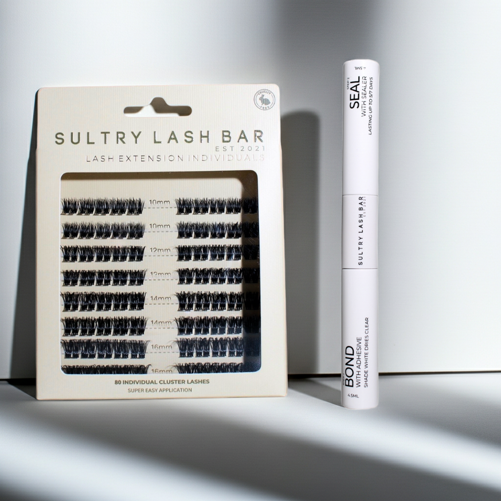 Sultry Lash Bar lash extension packaging with a tube of adhesive on a gray background