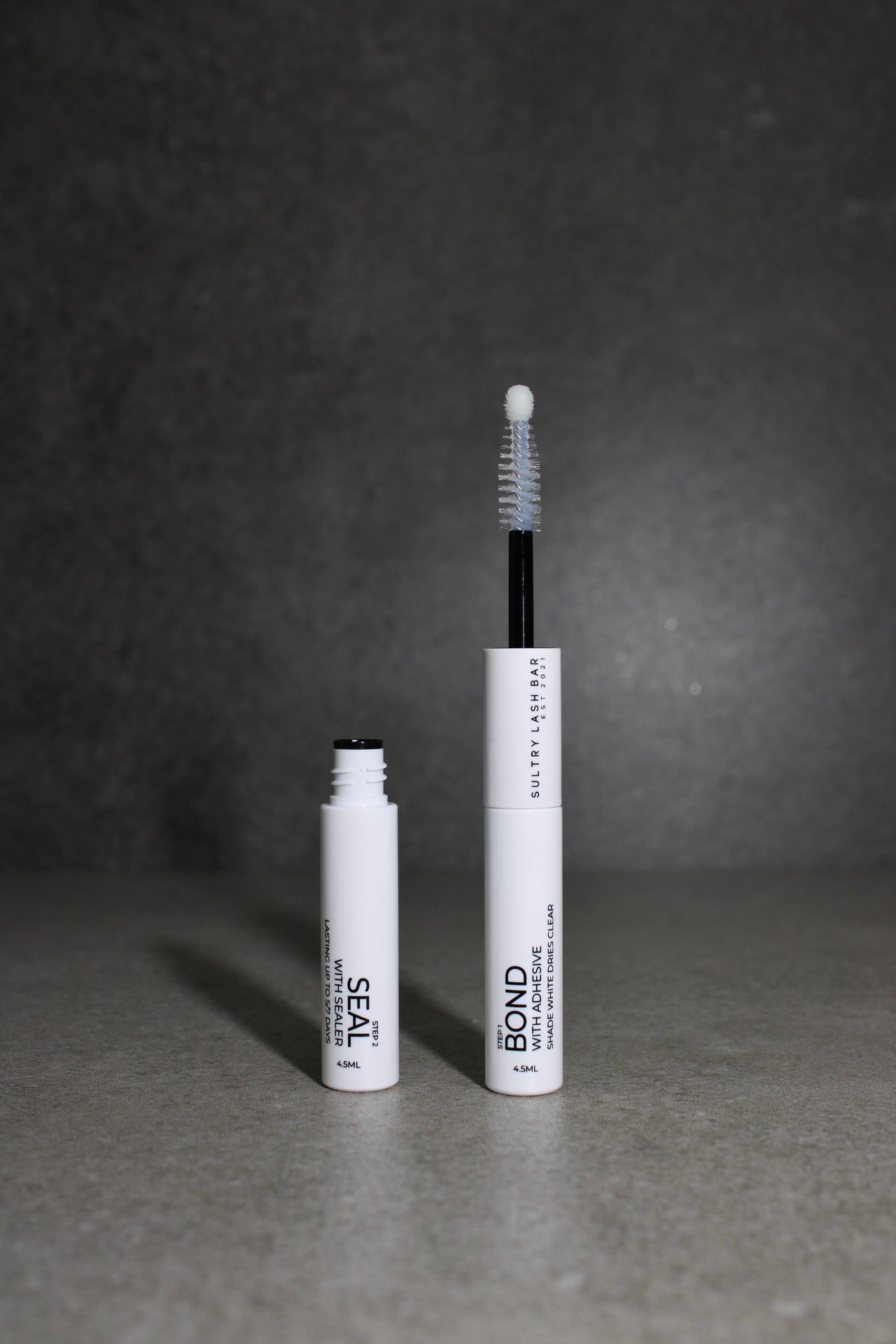 Two white mascara tubes with black text on a gray background
