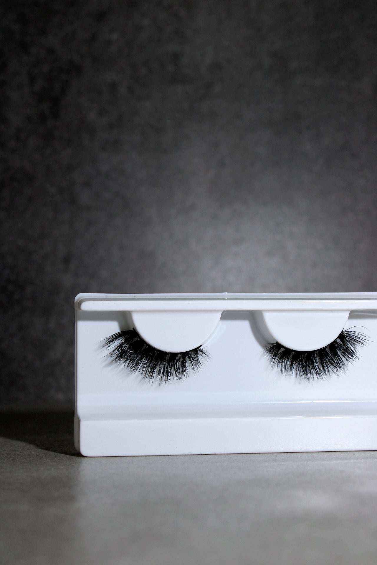 Pair of false eyelashes on a white tray against a dark background