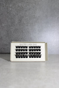 Eyelash extensions in a box with 'Sultry Lash Bar' branding on a gray background