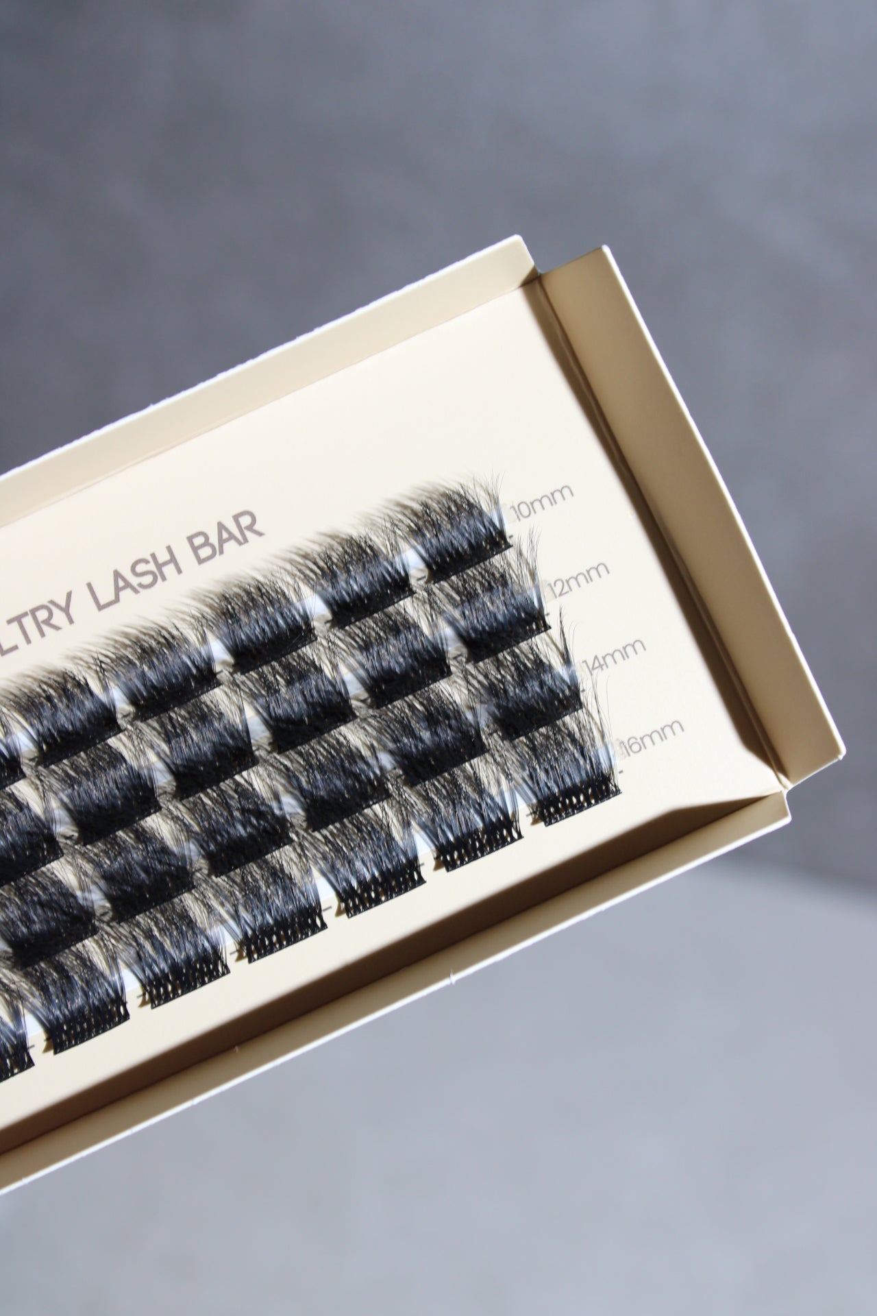 A box of false DIY single cluster individual eyelashes with varying lengths displayed in rows, labeled from 9mm to 14mm.