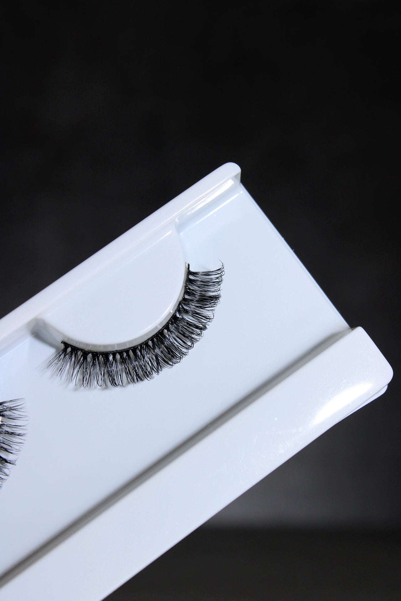 Pair of false eyelashes on a white tray against a black background