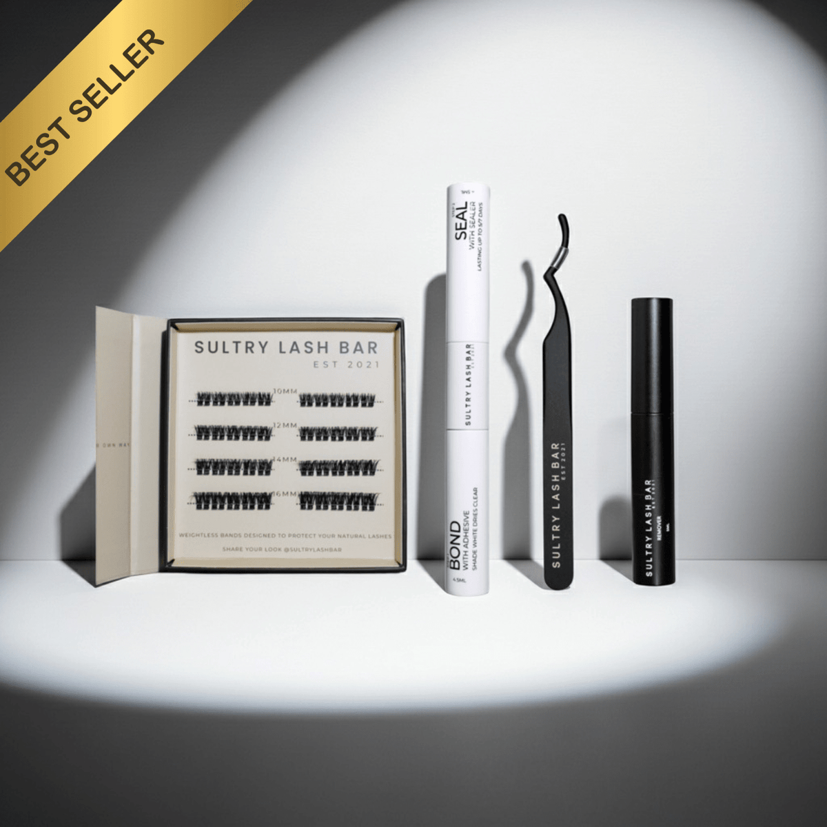 Eyelash products including a box of lashes, a tube of adhesive, and a curler on a white background.